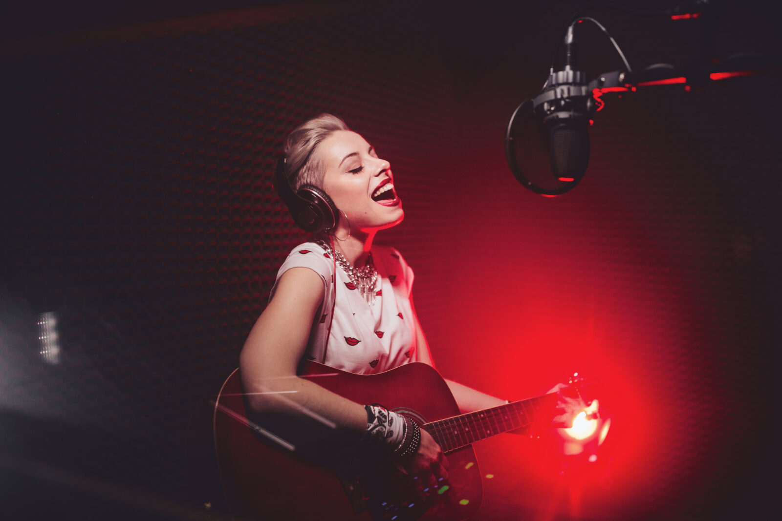 Fashionable hipster music artist playing the guitar and recording song in professional music studio